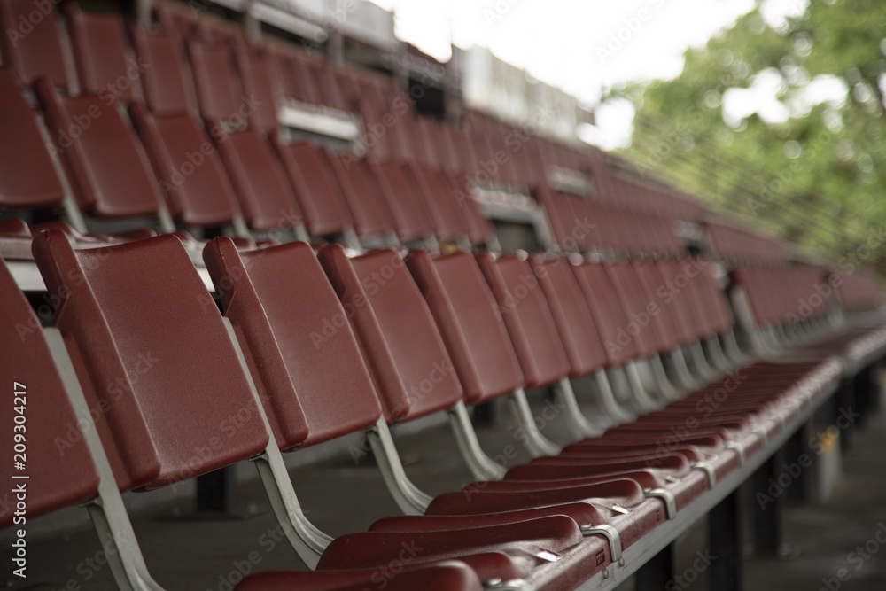 Rows of Empty Rust Colored Amphitheater Stadium Seats, Side Point of View with Pale Blue Sky and Trees in Background