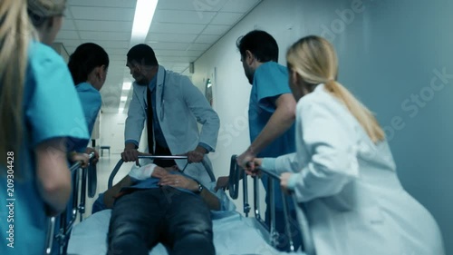 Emergency Department Doctors, Nurses and Surgeons Move Seriously Injured Patient Lying on a Gurney Through Hospital Corridors. Medical Staff in a Hurry Move Patient into Operating Theater. 