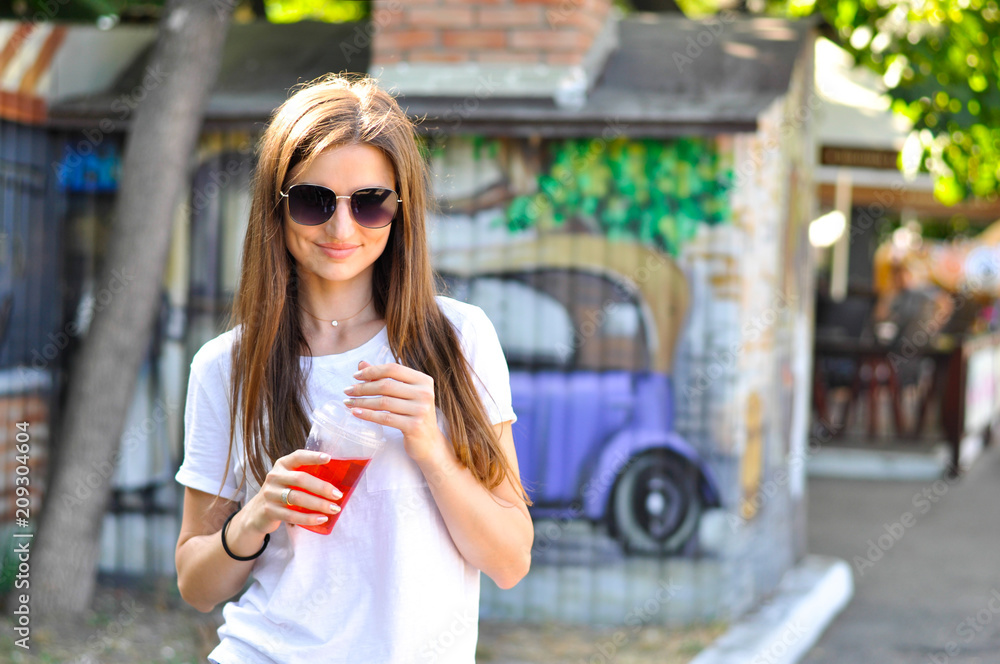 Fototapeta premium young attractive woman is walking around the city with a red cocktail (lemonade) in her hand