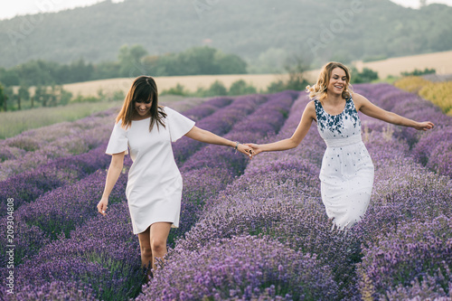 Beautiful sisters walking at lavender field, holding hands.