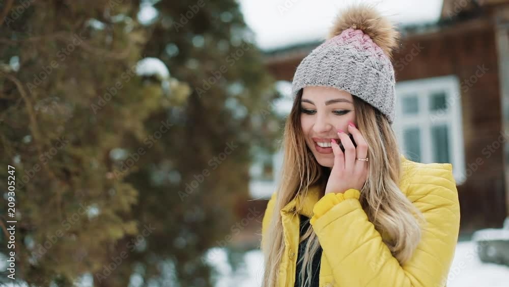 Smiling woman talks on the phone standing outside on the backyard under the falling snow. Woman Wearing A Winter Coat Near a Country House. Communication, Travel, Life Styles Concept. Shot on Red Epic Smiling woman talks on the phone standing outside on the backyard under the falling snow. Woman Wearing A Winter Coat Near a Country House. Communication, Travel, Life Styles Concept. Shot on Red Epic