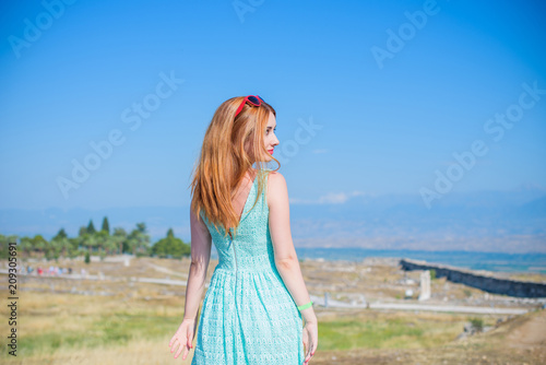 Girl tourist taking picture of Hierapolis in Turkey  Pamukkale  beautiful landscape with ruin  trees and mountain  woman in lace summer dress  