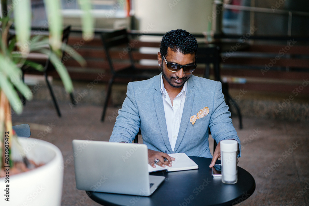 custom made wallpaper toronto digitalA millenial Indian Asian businessman is writing down ideas in his notebook. He is sitting in a coworking space with his laptop, smartphone, and a flask of coffee nearby.