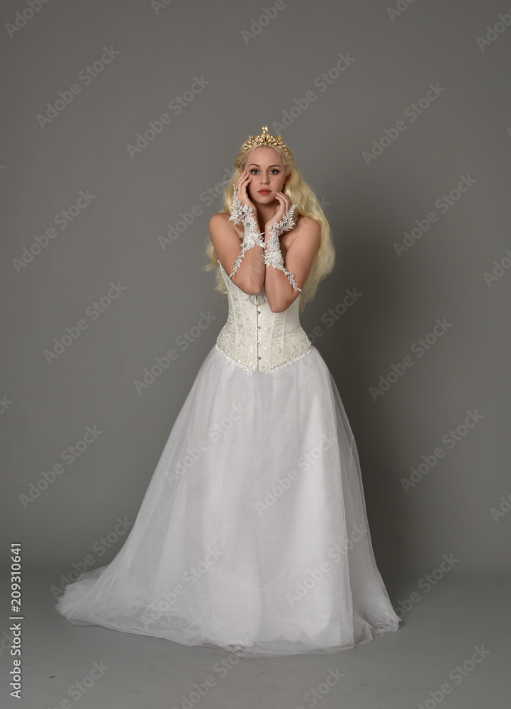 full length portrait of blonde girl wearing white corset gown. standing pose on grey studio background. full length portrait of blonde girl wearing white corset gown. standing pose on grey studio background.