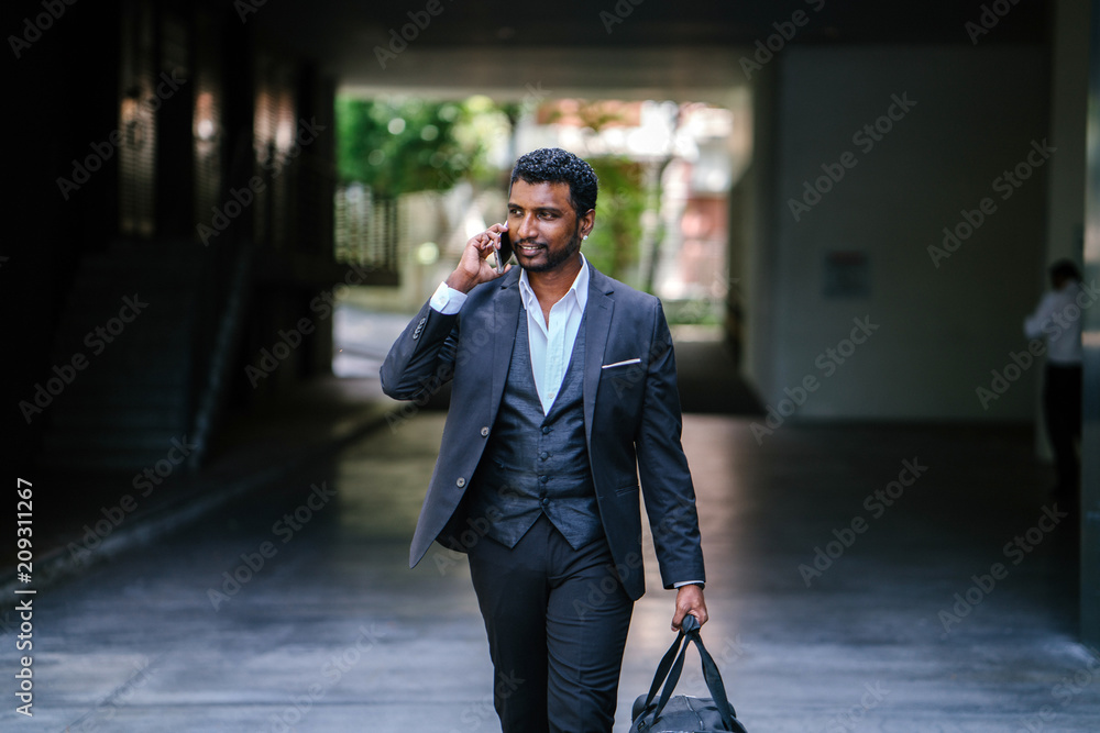 An attractive Indian Asian man is talking on his phone while walking toward his car. He is wearing stylish clothes and is carrying a gym bag on his left hand. An attractive Indian Asian man is talking on his phone while walking toward his car. He is wearing stylish clothes and is carrying a gym bag on his left hand.
