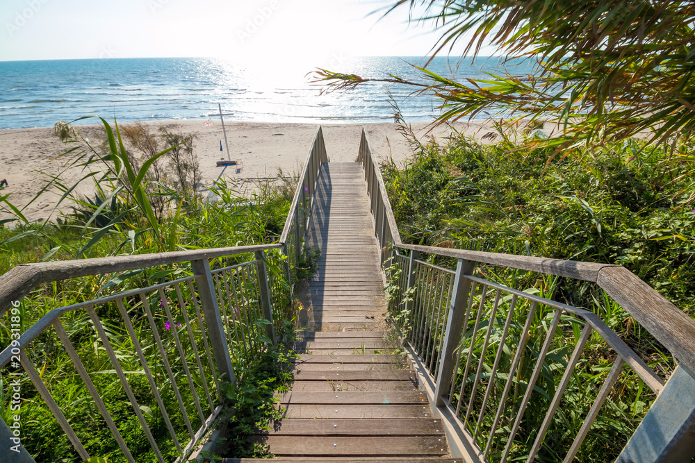 Obraz premium Wooden stairs leading off the cliff onto the sand on a sunny day, Wooden board walk stairs