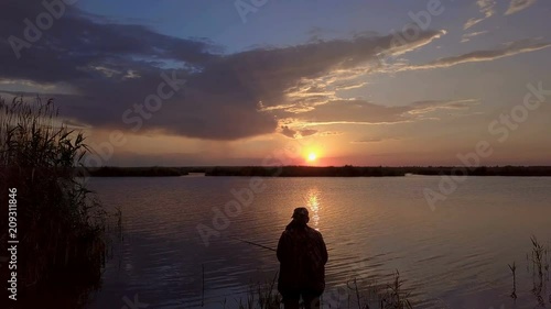 Aerial View. A man is fishing on the background of the setting sun. Beautiful evening light. 4K photo