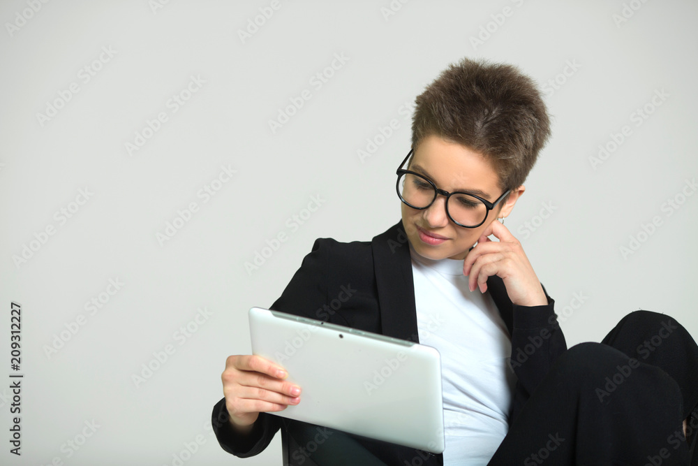 young beautiful girl with short hair on her head, in a suit and glasses with a tablet in her hands young beautiful girl with short hair on her head, in a suit and glasses with a tablet in her hands