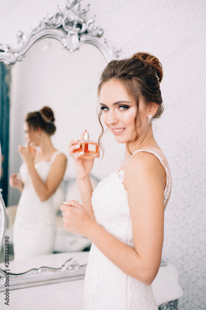 The bride is holding perfume and looking in the mirror. Morning of the bride The bride is holding perfume and looking in the mirror. Morning of the bride