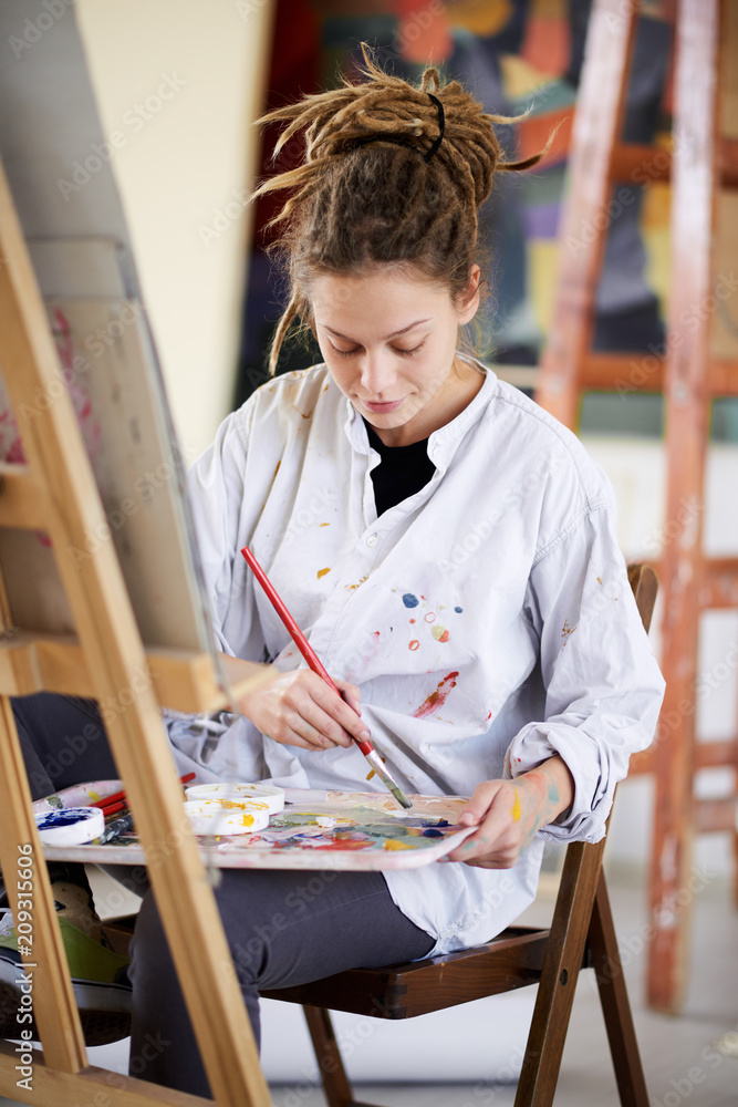 Artistic girl sitting in studio and paint on easel.