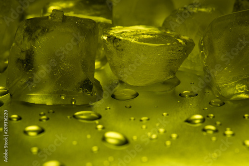 Ice cubes in lemon color on a reflecting table with drops of water