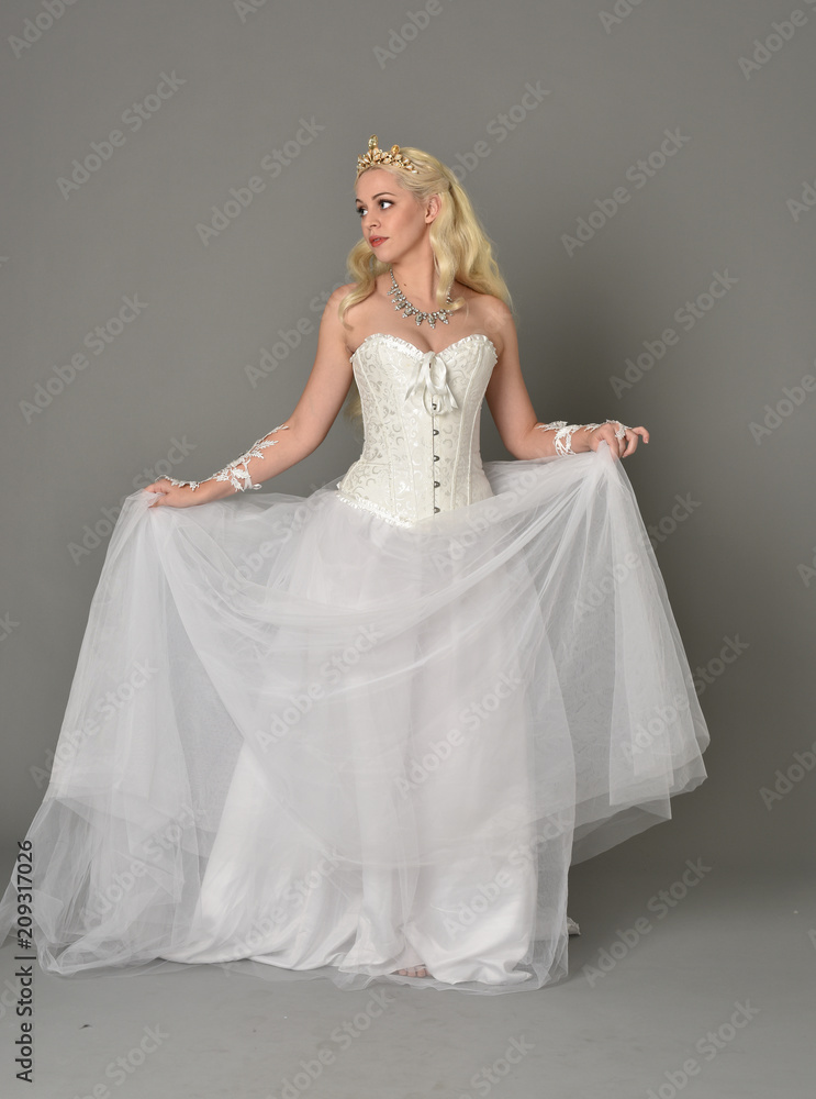 full length portrait of blonde girl wearing white corset gown. standing pose on grey studio background. full length portrait of blonde girl wearing white corset gown. standing pose on grey studio background.