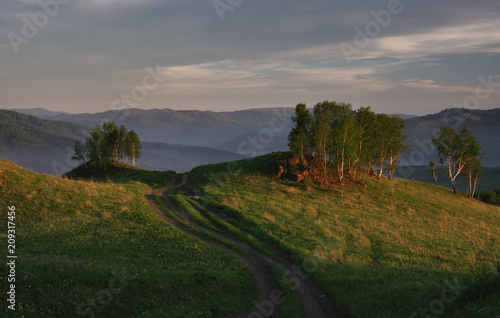 Country dirt road on the hill up on the background of the sunset mountains