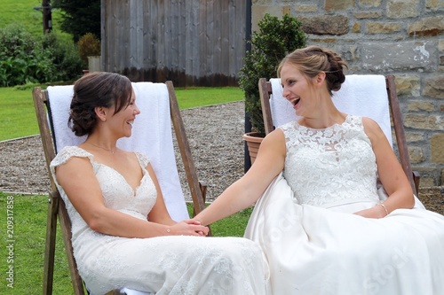 Same sex brides talking and sat on deck chairs at the end of their wedding day 