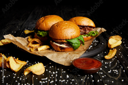 Tasty hamburgers and french fries with ketchup on wooden board