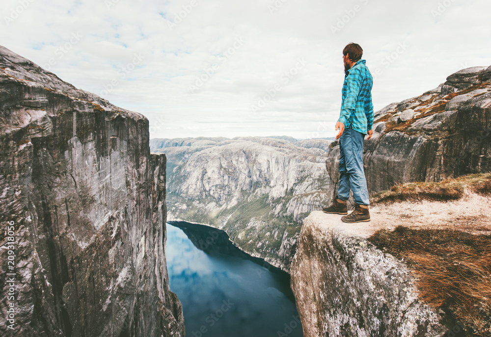 Explorer man standing on cliff over fjord solo traveling hike in Norway adventure lifestyle weekend getaway trip Kjerag rocky mountains