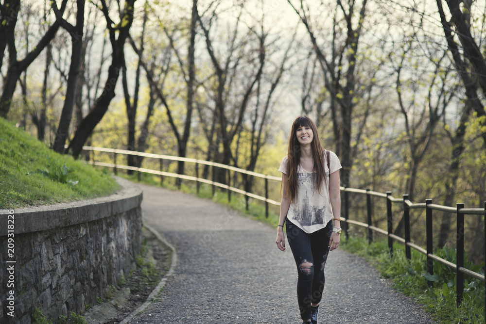 beautiful young woman walking outside in the park  . Caucasian girl with long brown hair smiling