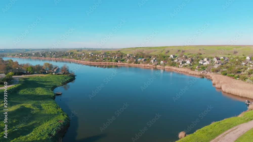 The flight of drones over country houses in the hills on the shore of the pond early in the morning at dawn. Flight over the water at a bird's eye view. Aerial view 4K The flight of drones over country houses in the hills on the shore of the pond early in the morning at dawn. Flight over the water at a bird's eye view. Aerial view 4K