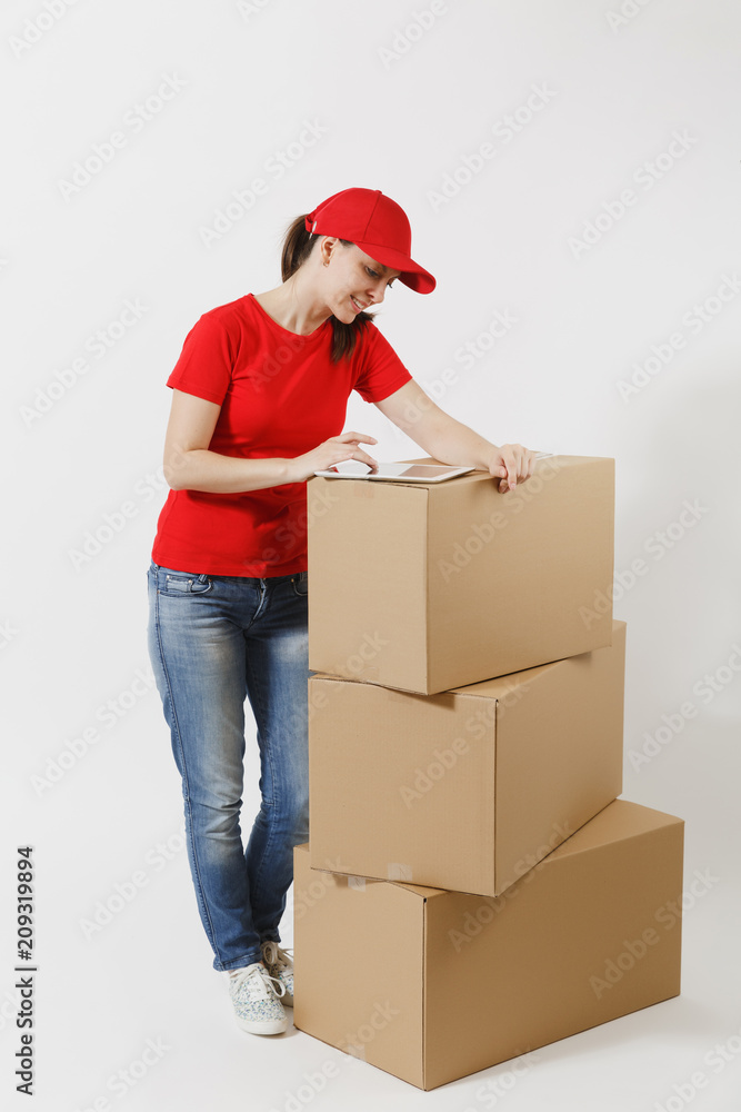 Full length portrait of delivery young woman in red cap, t-shirt isolated on white background. Female courier standing near empty cardboard boxes with tablet pc computer. Receiving package. Copy space Full length portrait of delivery young woman in red cap, t-shirt isolated on white background. Female courier standing near empty cardboard boxes with tablet pc computer. Receiving package. Copy space