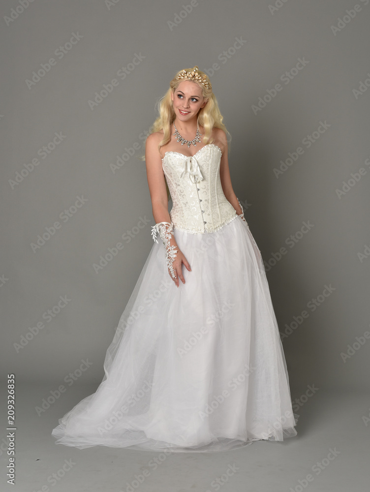 full length portrait of blonde girl wearing white corset gown. standing pose on grey studio background. full length portrait of blonde girl wearing white corset gown. standing pose on grey studio background.
