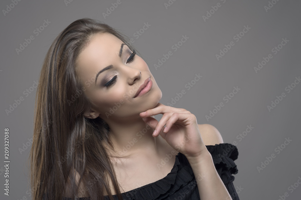 Relaxed mixed race tanned latin beauty with hand on chin and perfect skin complexion looking down against gray studio background. Relaxed mixed race tanned latin beauty with hand on chin and perfect skin complexion looking down against gray studio background.