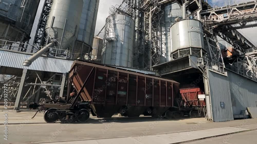 Freight train with agricultural crops as cargo transportations moving at big grain terminal near sea. Unloading grain from railway carriage to elevator. Grain transshipment facility hub silo. Freight train with agricultural crops as cargo transportations moving at big grain terminal near sea. Unloading grain from railway carriage to elevator. Grain transshipment facility hub silo.