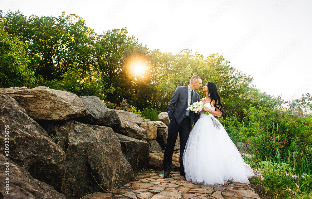 couple, bride and groom are walking in the park with greenery and stones on a sunny day couple, bride and groom are walking in the park with greenery and stones on a sunny day