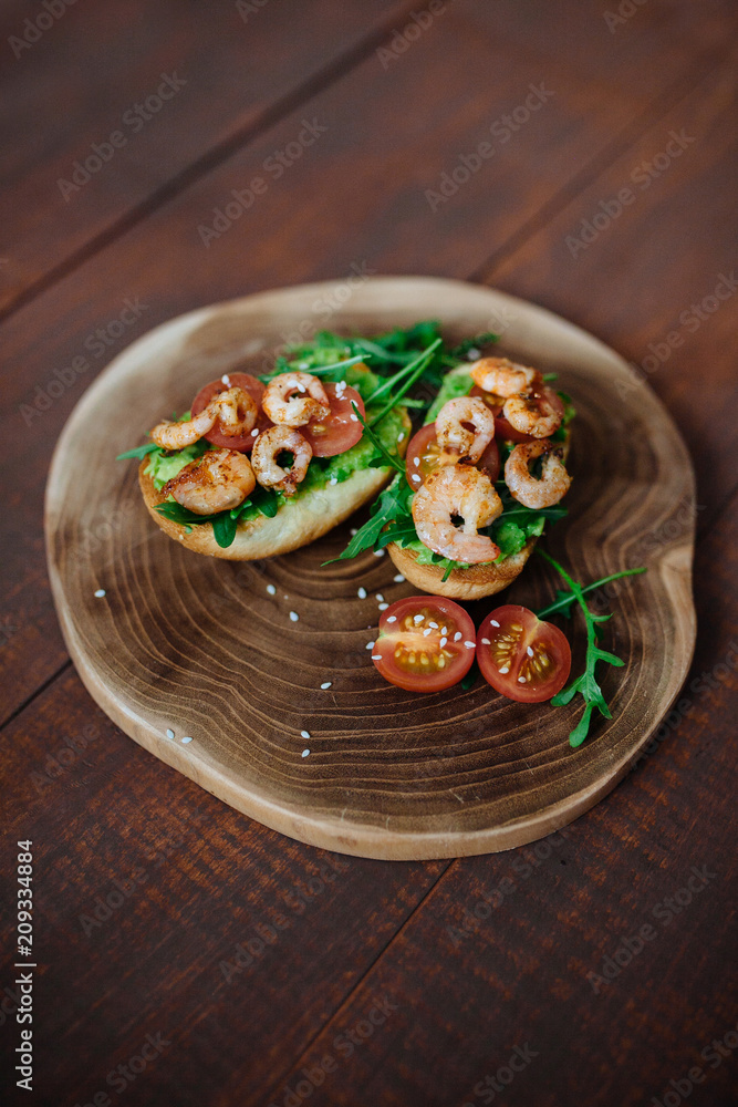 Tasty snack of open sandwich with avocado, shrimps and arugula on wooden cutting board. Top view.Breakfast concept