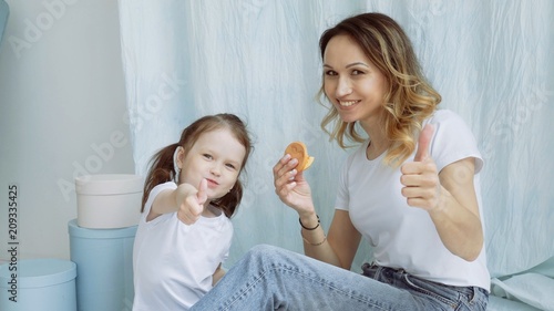 Attractive young woman with her daughter is cooking in the kitchen. Young Mom with daughter sitting on the floor with cookies in hands showing LIK. photo