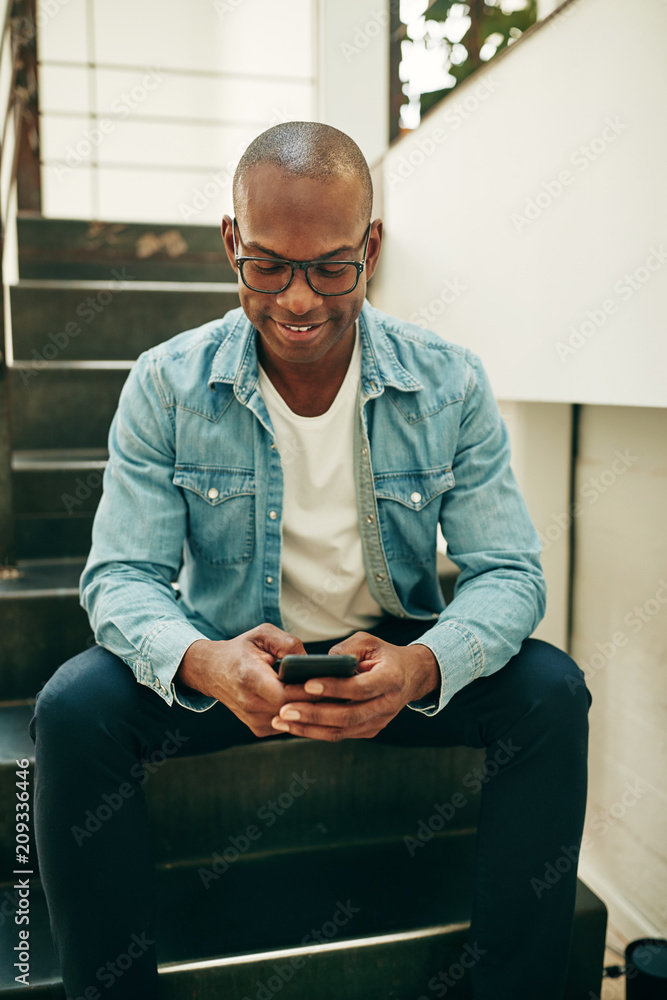 Young African businessman sitting on office stairs reading text