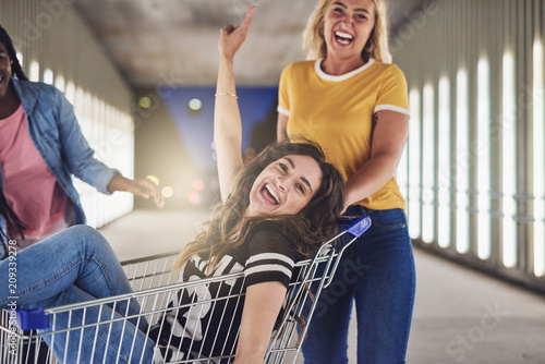 Girlfriends playing with a shopping cart together in the city
