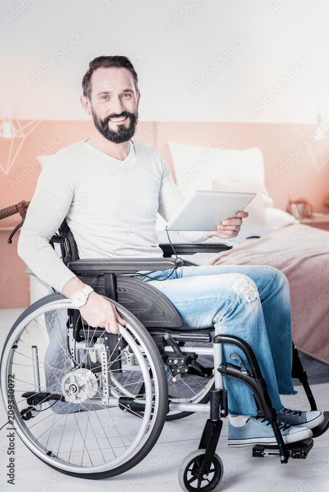 I feel happy. Joyful handicapped man sitting in a wheelchair and holding a tablet I feel happy. Joyful handicapped man sitting in a wheelchair and holding a tablet