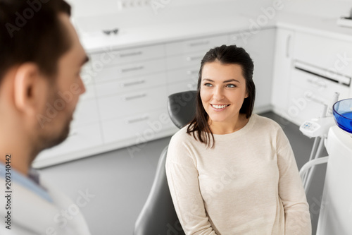 medicine, dentistry and healthcare concept - smiling female patient talking to dentist at dental clinic office