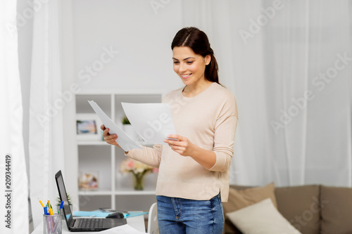 people, freelance and education concept - happy woman with papers and laptop working or learning at home