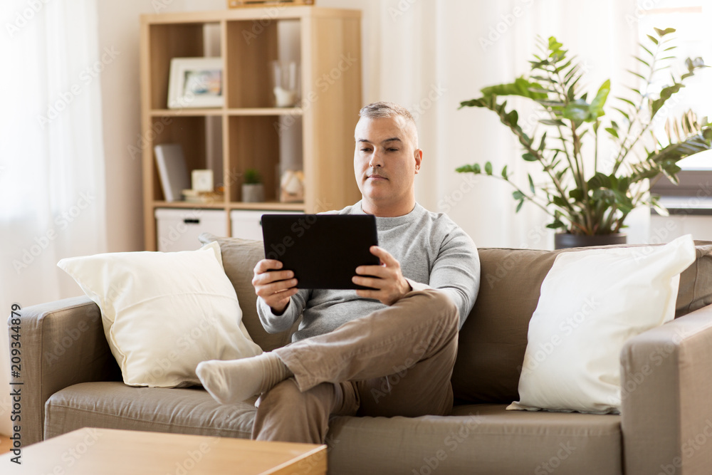 technology, people and lifestyle concept - man with tablet pc computer sitting on sofa at home technology, people and lifestyle concept - man with tablet pc computer sitting on sofa at home