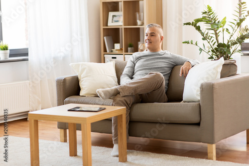 leisure and people concept - happy middle-aged man sitting on sofa at home