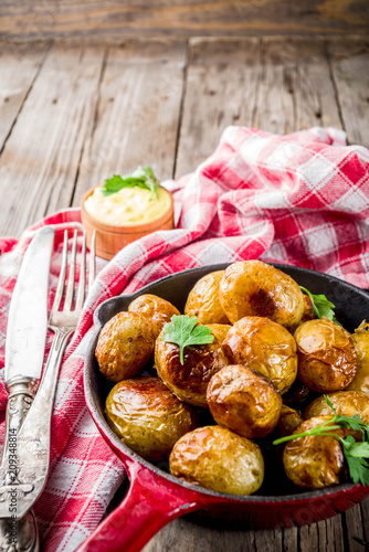 Baked in frying pan whole young potatoes, homemade vegetarian food, wooden old rustic table, with sauce, copy space