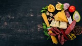 Assortment of sausage, cheese and fresh vegetables. Italian cuisine. On a black wooden background. Top view. Copy space.