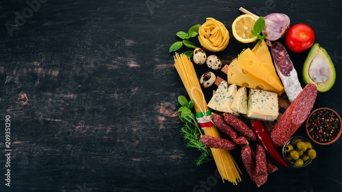 Assortment of sausage, cheese and fresh vegetables. Italian cuisine. On a black wooden background. Top view. Copy space.