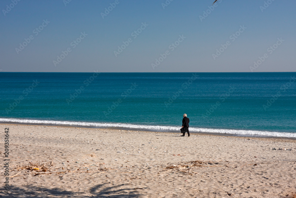 A person walks by the sea on a deserted beach