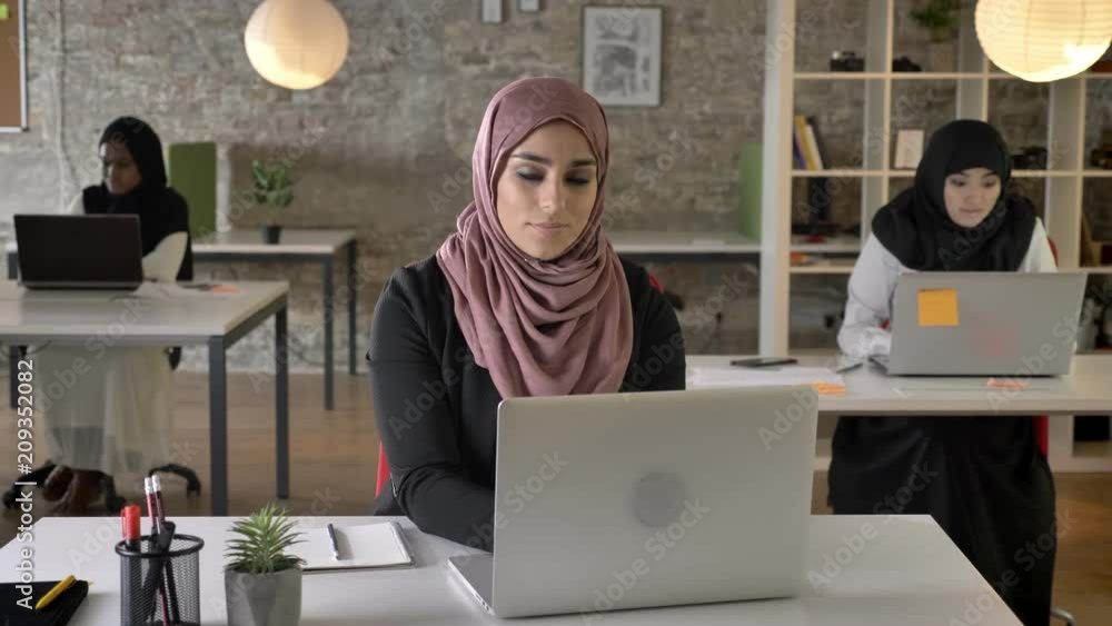 Three young muslim womans in hijab sitting and working in modern office ...