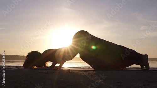 A silhouette footage of a woman who is doing Urdhva Mukha Shvansana on the beach. Backbend. Sun shines on the background photo