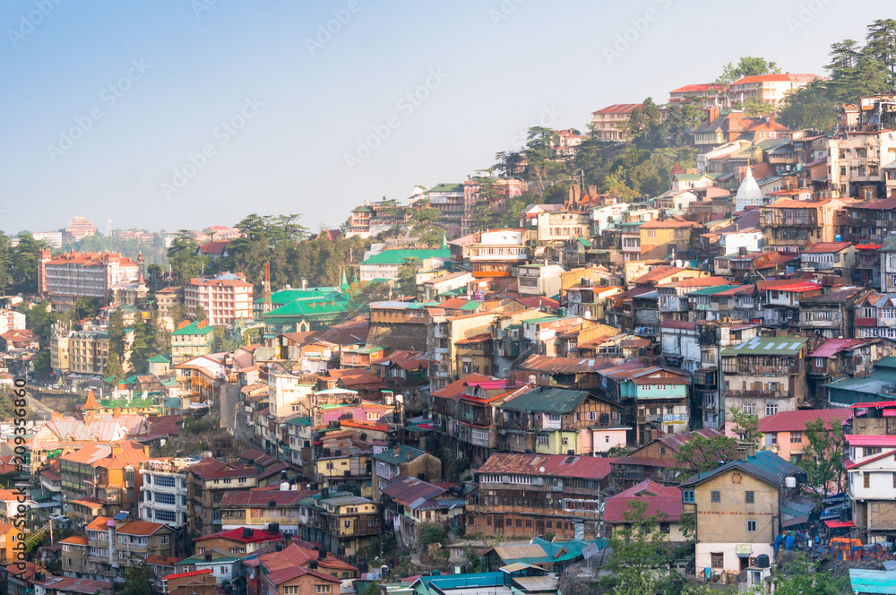 Colorful buildings on the side of a mountainside on a dawn morning. Shot in shimla it shows the sloping roof buildings with trees in between