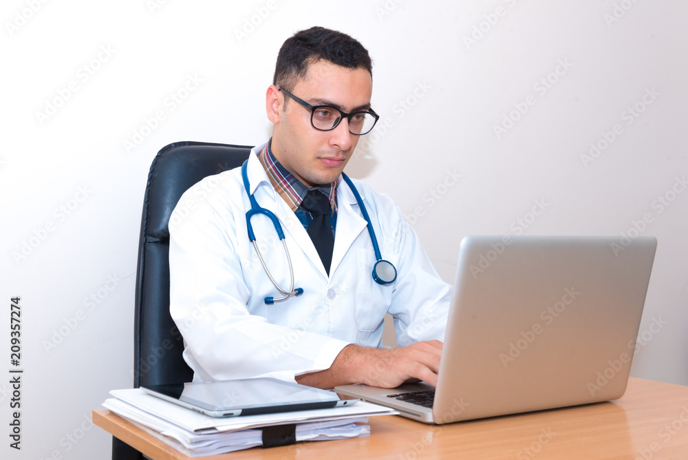 Doctor sitting at the desk, using laptop typing and searching data from the internet or searching patient record data. Doctor sitting at the desk, using laptop typing and searching data from the internet or searching patient record data.