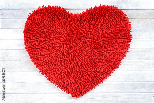 Red heart shape cleaning feet doormat or carpet texture on white wooden background.