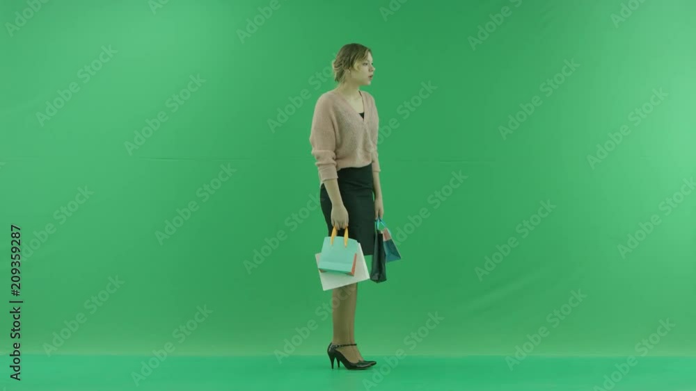 Pretty shopping woman with shopping bags. Female shopper holding shopping bags sideways on green background in studio. Pretty shopping woman with shopping bags. Female shopper holding shopping bags sideways on green background in studio.