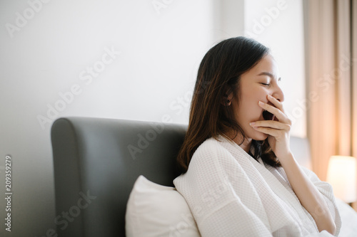Young woman sitting on the bed and yawning photo