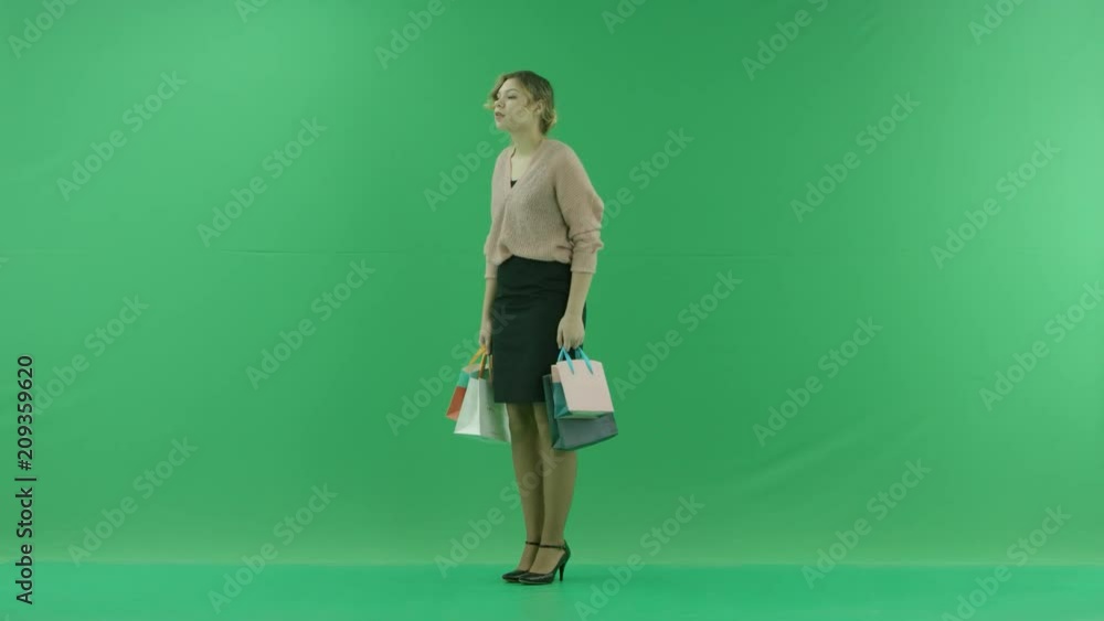 Pretty shopping woman with shopping bags. Female shopper holding shopping bags half-turned on green background in studio. Pretty shopping woman with shopping bags. Female shopper holding shopping bags half-turned on green background in studio.