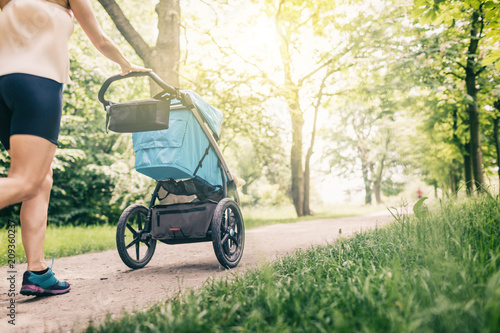 Running woman with baby stroller enjoying summer in park photo