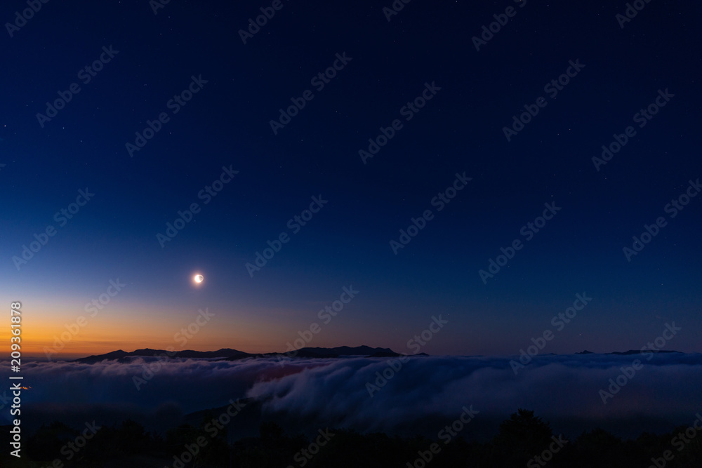 Quarto di Luna nel cielo sereno all’alba sopra una distesa di nuvole bianche
